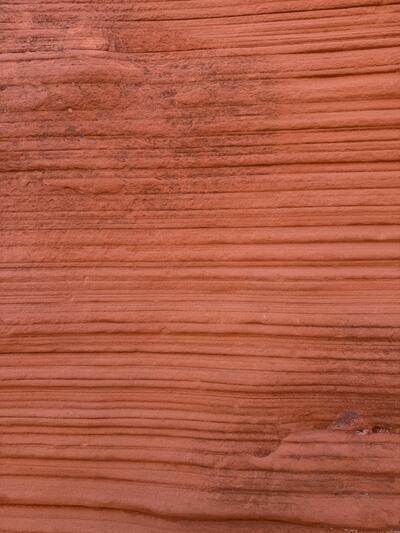 A close-up of a sandstone wall, filling the frame with horizontal bands of terracotta and salmon-colored rock. Fine parallel layers of sediment ripple across the surface like wood grain.